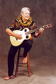 a picture of keola on a stool with a guitar